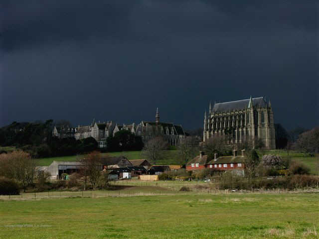 Atmoshpheric photograph of Lancing College brightly lit with storm clouds behind.